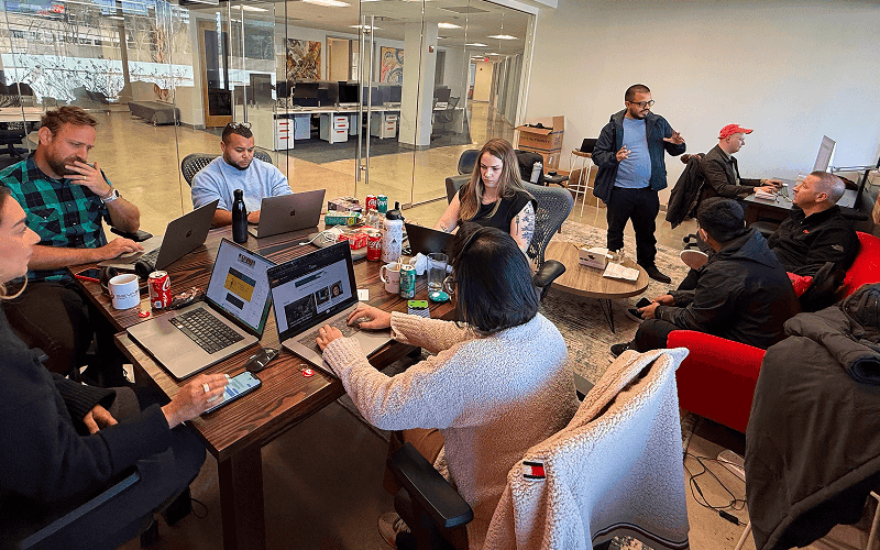A diverse group of people working and discussing around a table in a modern office space.
