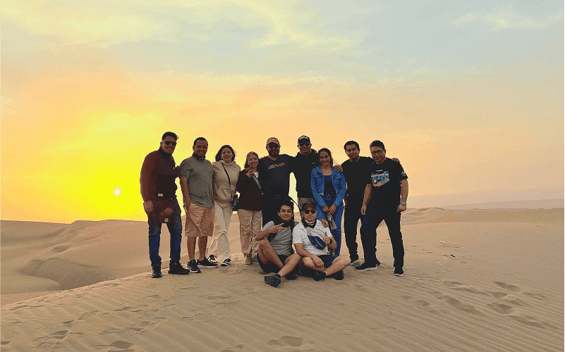Punch Team Culture Photo-31 A group of ten people poses together on a desert dune at sunset.