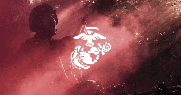 A soldier in a helmet raises his hand in front of a smoky background with a white Marine Corps emblem overlay.