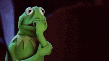 A green puppet frog with large eyes and a finger to its lips, suggesting silence or secrecy.